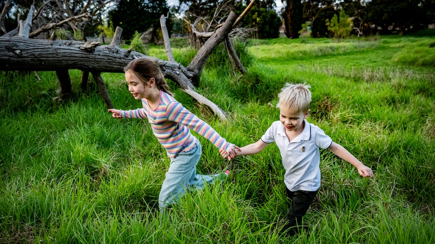 Two young white kids holding hands, running through long grass