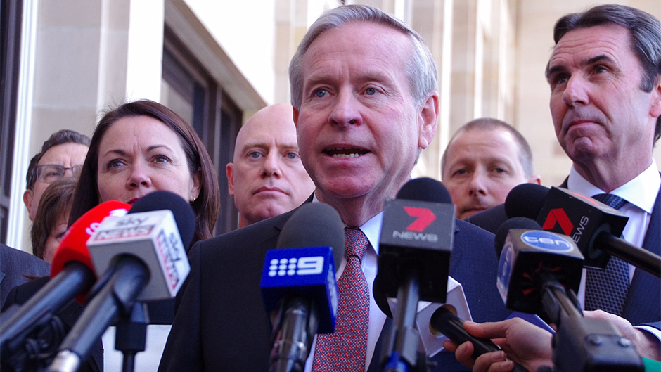 Colin Barnett speaks into microphones with fellow Liberal MPs behind him.
