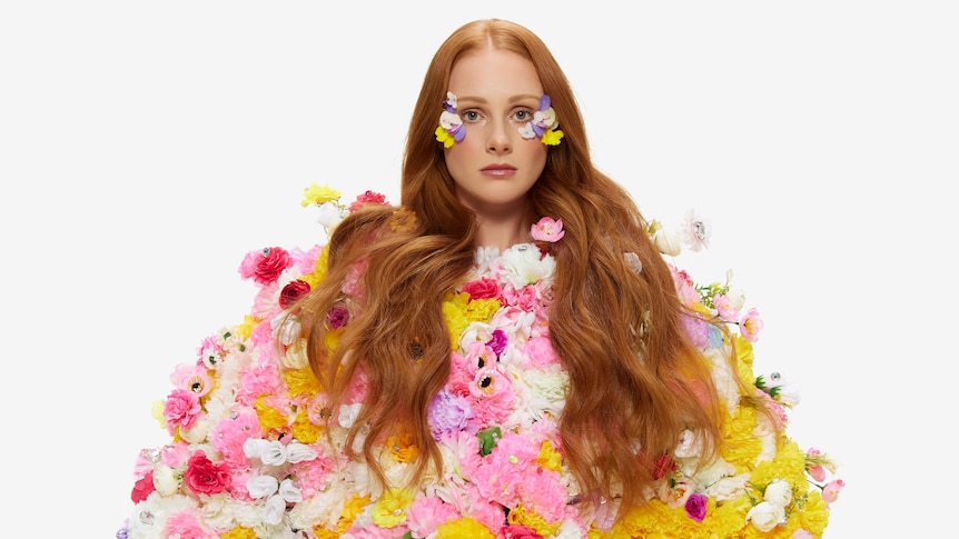 Vera Blue draped in colourful flowers in he hair and dress against a white background