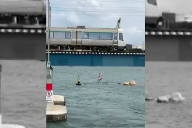 A screen shot from recorded footage showing a man jumping from the top of a train into a river.