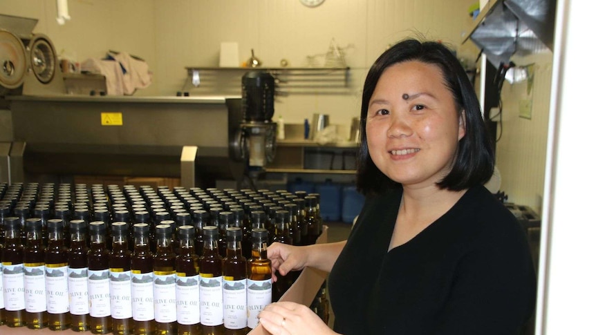 A woman standing beside bottles of olive oil