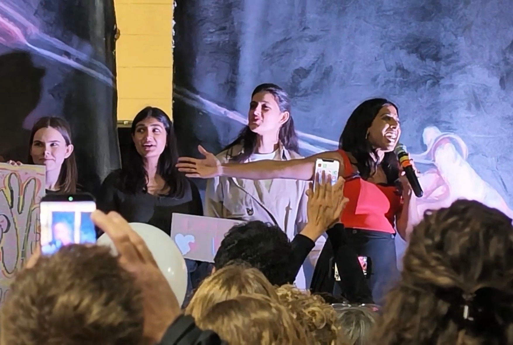 Joanna speaks into a microphone and gestures strongly with her arm.
