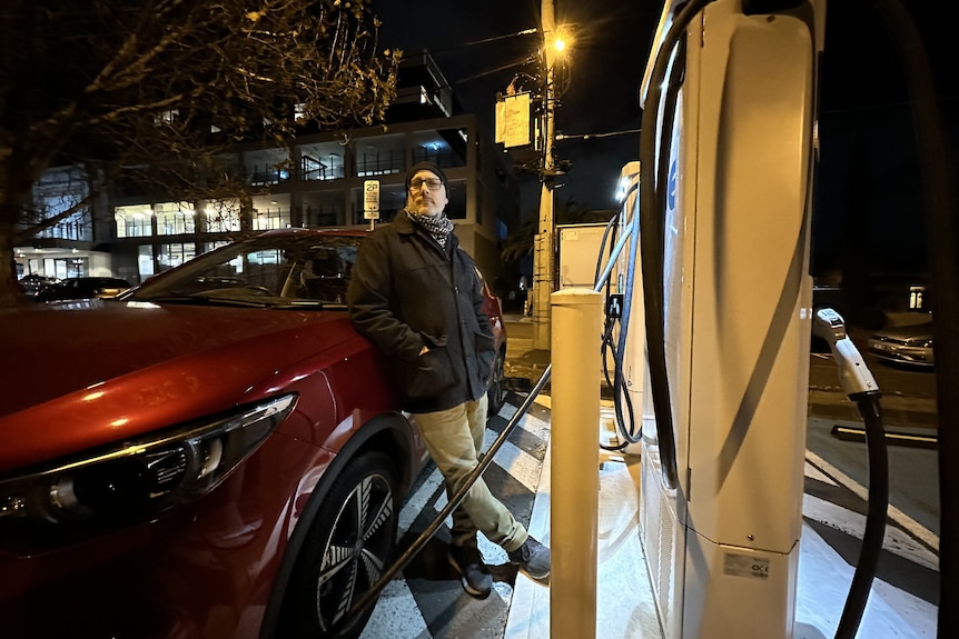 Michael Bond stands in front of a red car at a charging station.