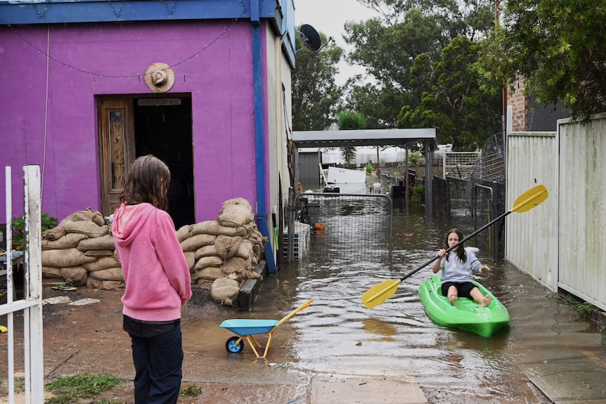 Children paddling canoes in a driveway.
