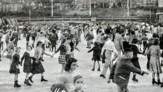 A large crowd skating on an open ice rink.