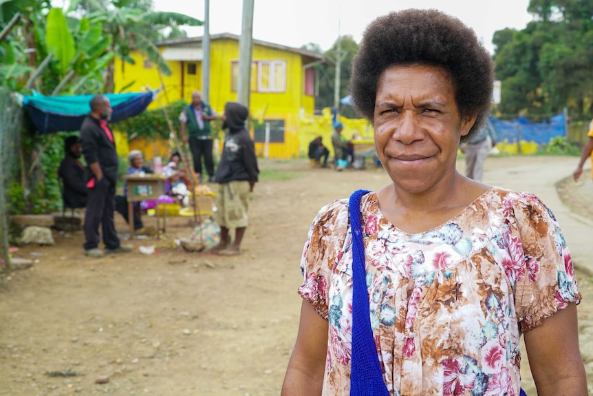 A woman in a floral top standing outside a bright yellow building in PNG