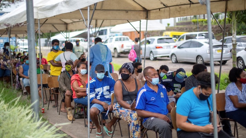 Residents wear masks as they sit and wait outside a vaccination centre in Suva