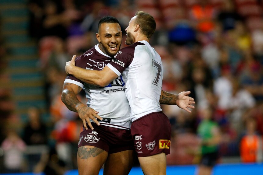 A rugby league player is embraced by a teammate after scoring a try
