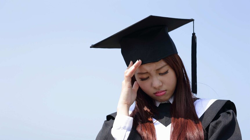 A woman in graduate clothing and cap with her head in her hands