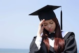 A woman in graduate clothing and cap with her head in her hands