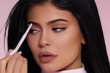 Kylie Jenner uses a pink eyebrow marker to apply make-up to her face.