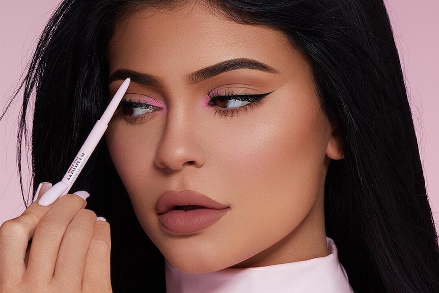 Kylie Jenner uses a pink eyebrow marker to apply make-up to her face.