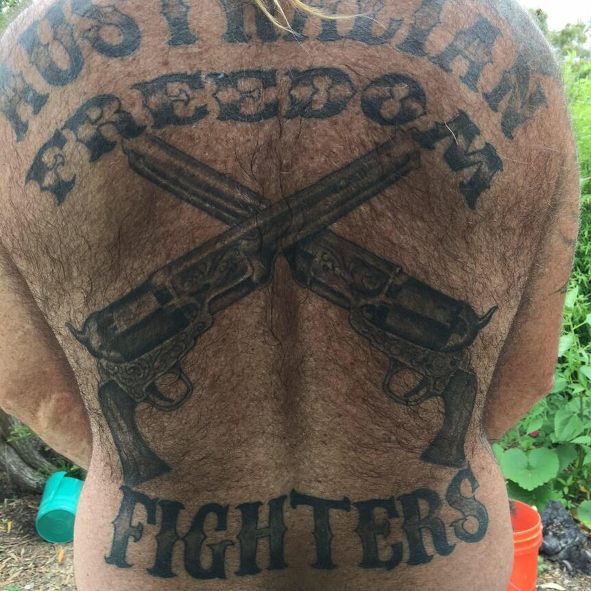 A full back tattoo showing the words 'Australian freedom Fighters' with two guns crossed in the centre.