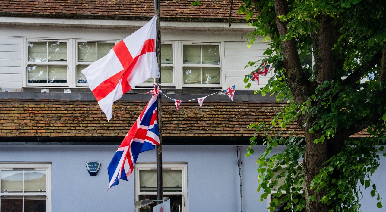 Two flag flying near a building.