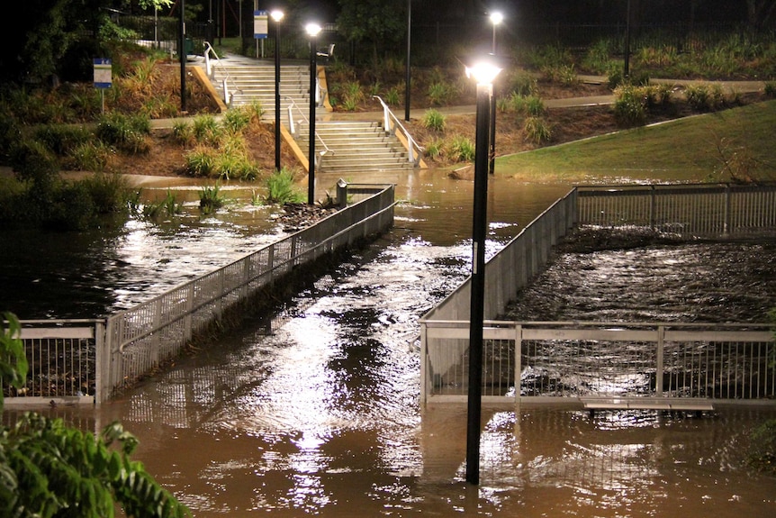 A flooded Kedron Brook flows over a foot bridge over the brook at Lutwyche in Brisbane.