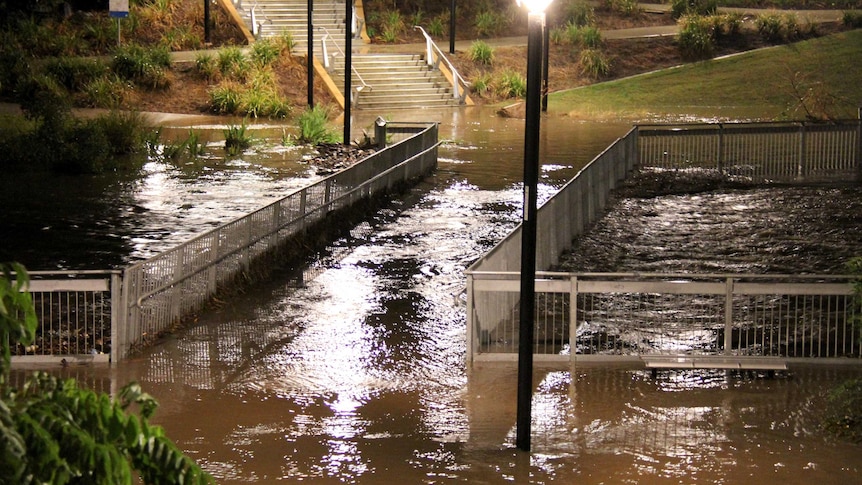A flooded Kedron Brook flows over a foot bridge over the brook at Lutwyche in Brisbane.
