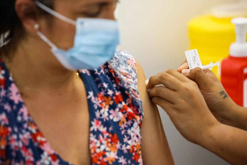 A woman wearing a face mask receives a COVID-19 vaccine.