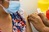 A woman wearing a face mask receives a COVID-19 vaccine.