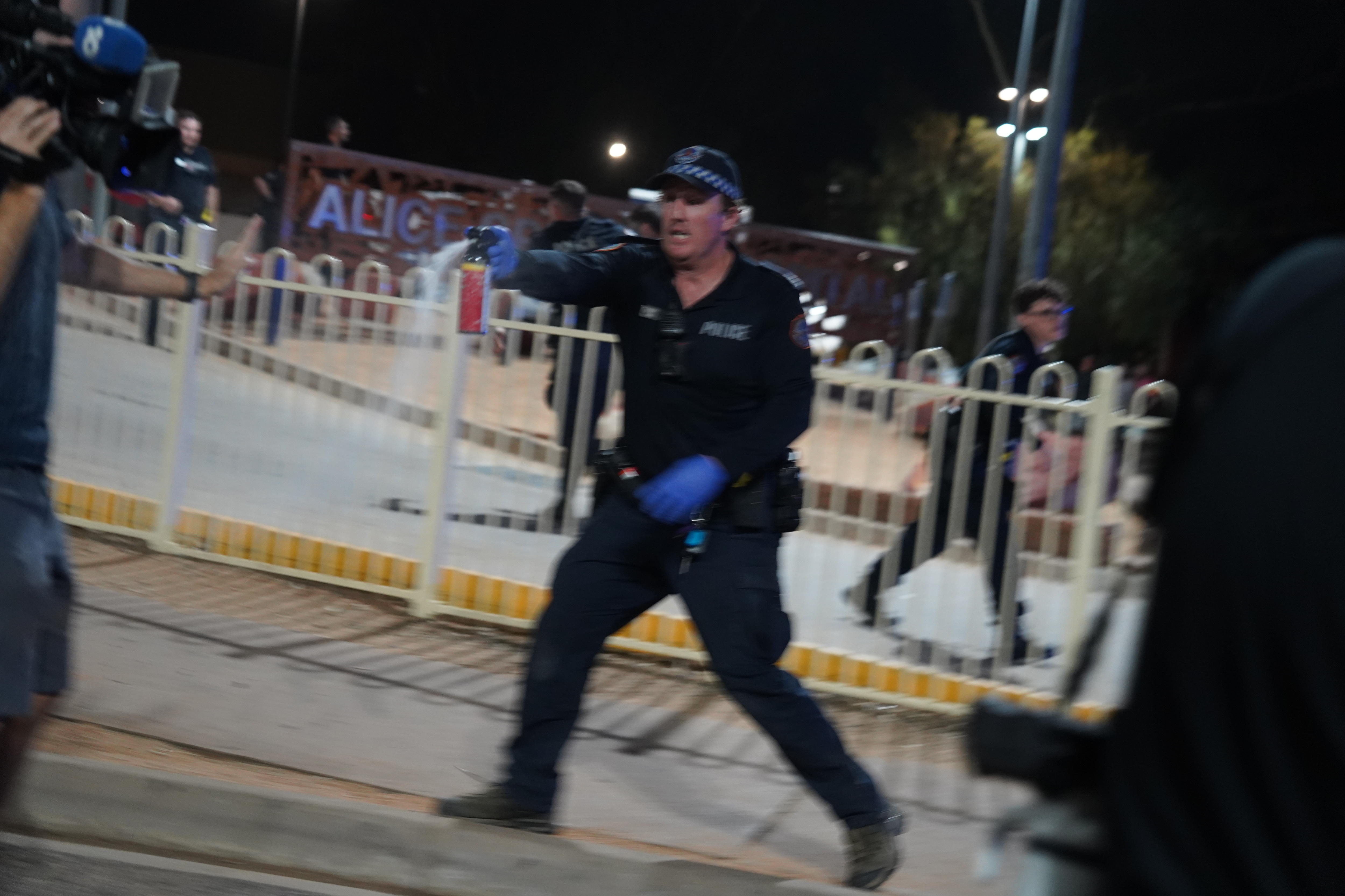 Un oficial de policía del Territorio del Norte usa gas pimienta en una calle por la noche.