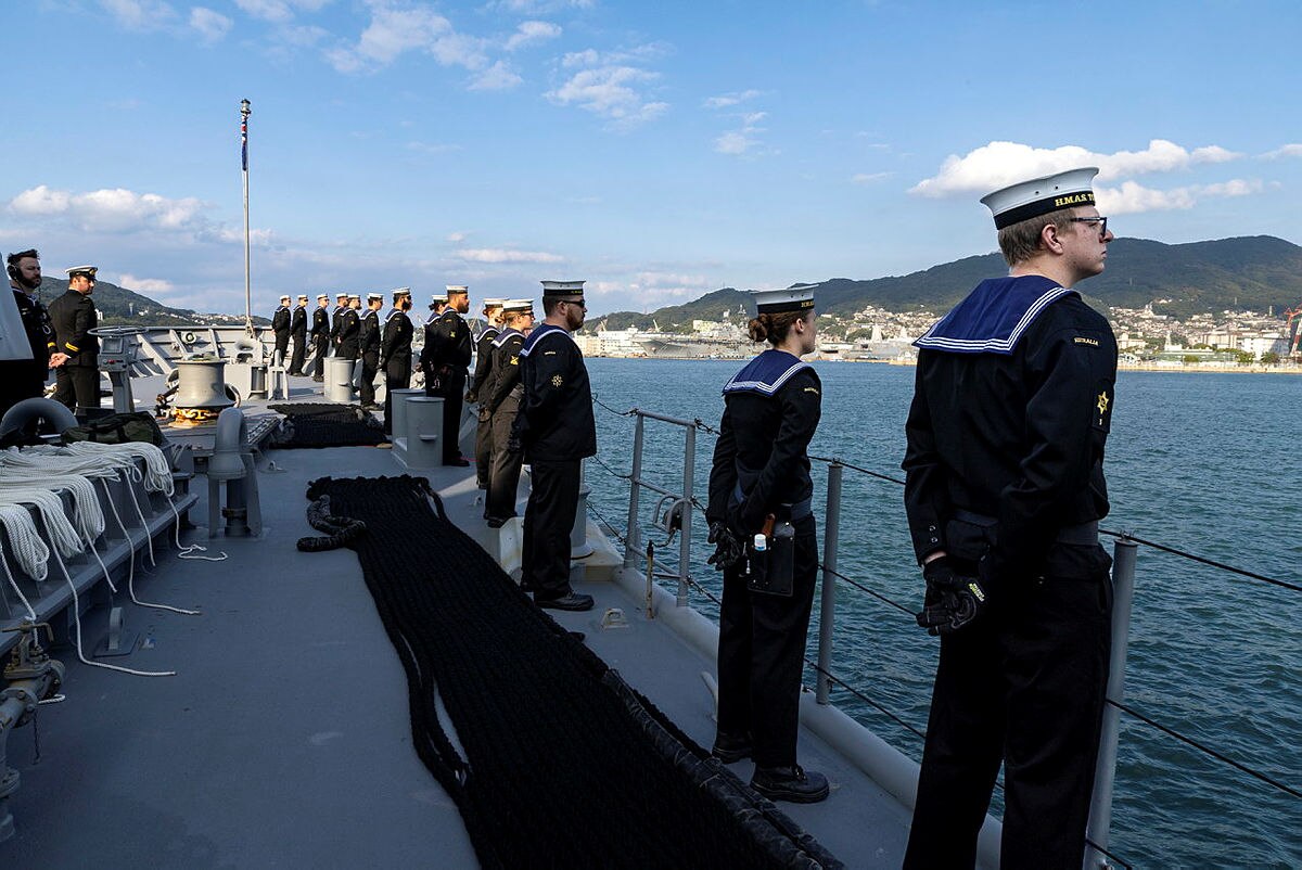 Naval personnel stand on the ship HMAS Toowoomba, looking out to sea during a deployment in Japan