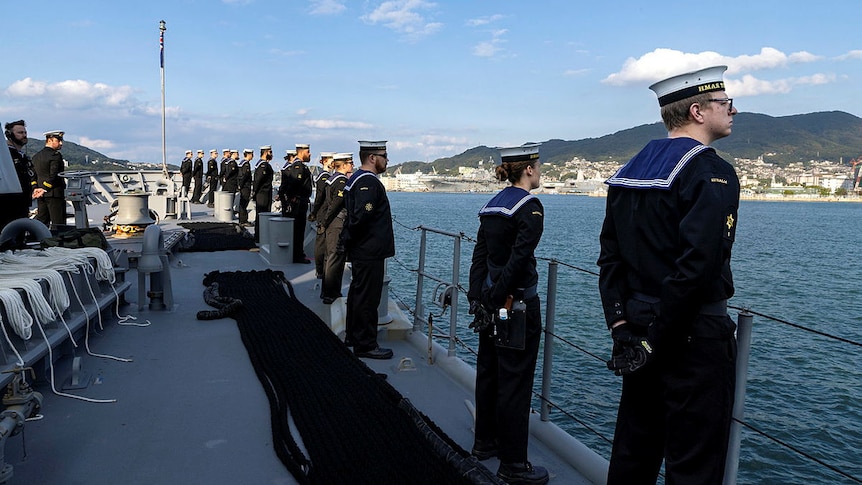 Naval personnel stand on the ship HMAS Toowoomba, looking out to sea during a deployment in Japan