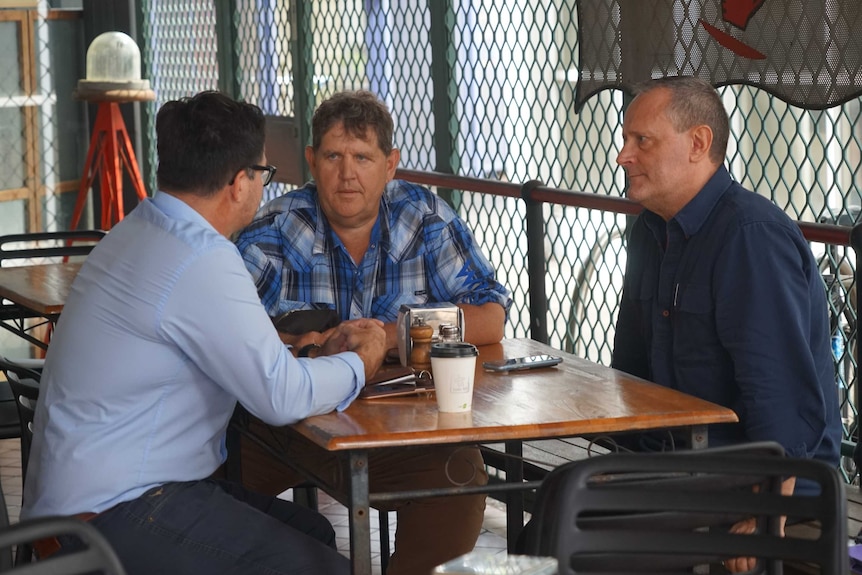 Three men sitting at a cafe table.