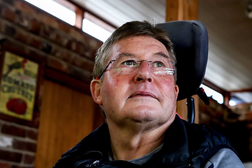 Man with glasses stares toward window sitting in wheelchair with brick wall behind him