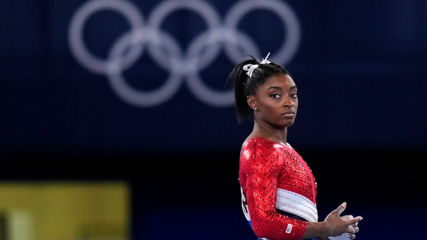 dark haired woman in red leotard clasps hands