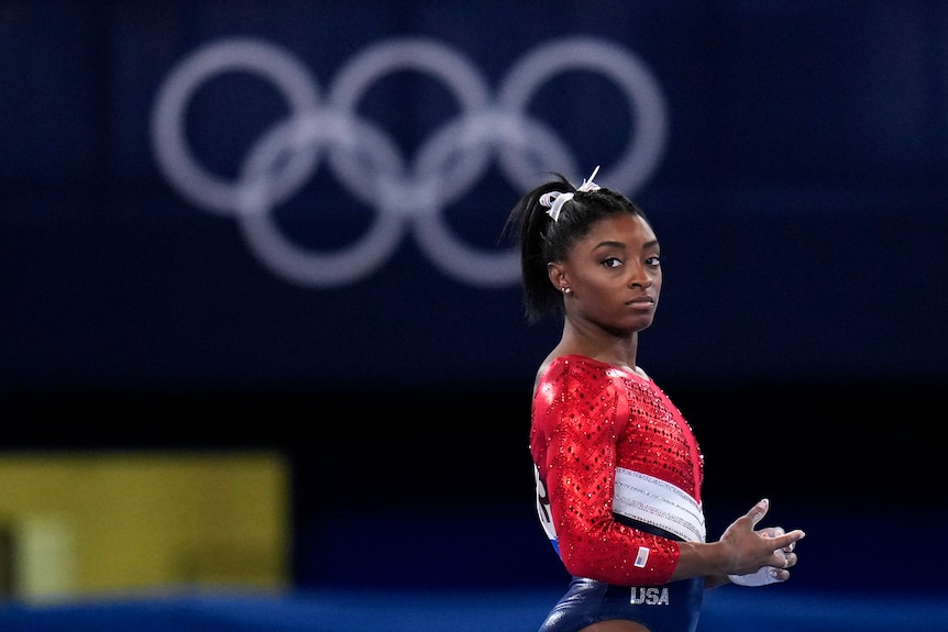 dark haired woman in red leotard clasps hands