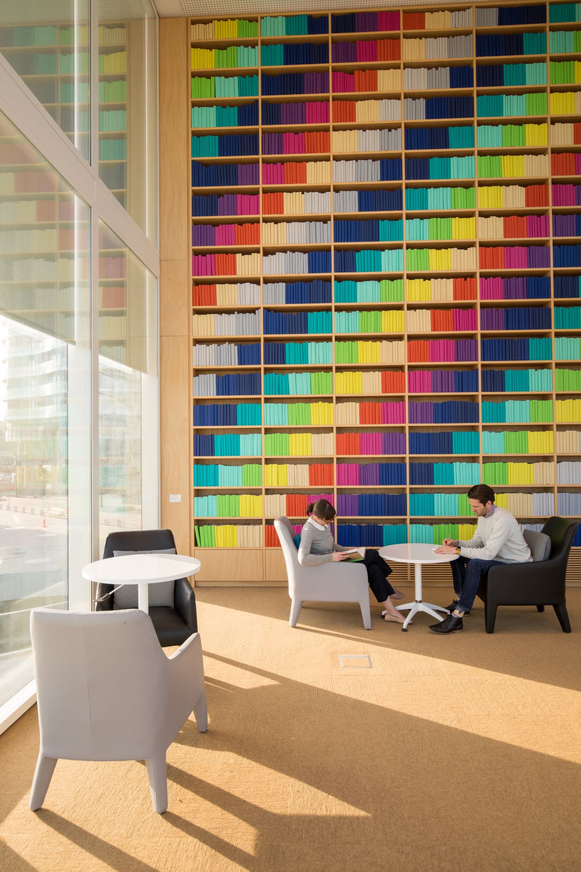 Two people sit next to bookshelves with many colourful books.