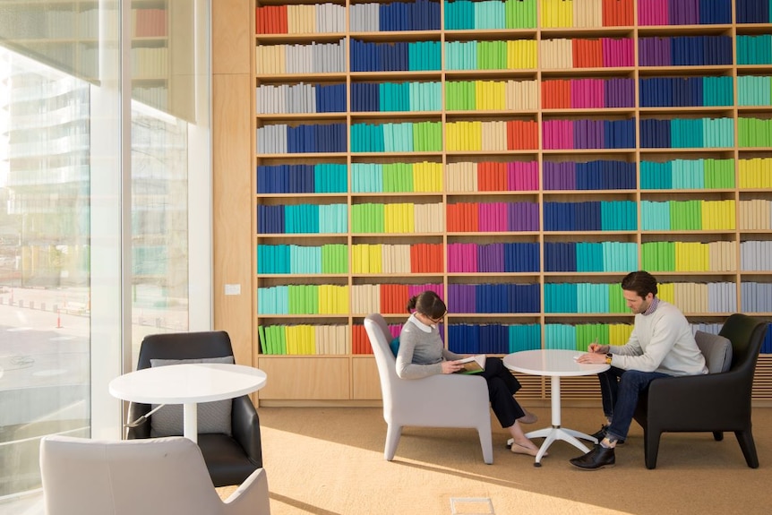 Two people sit next to bookshelves with many colourful books.