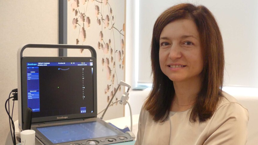 A woman smiles in front of an ultrasound screen.