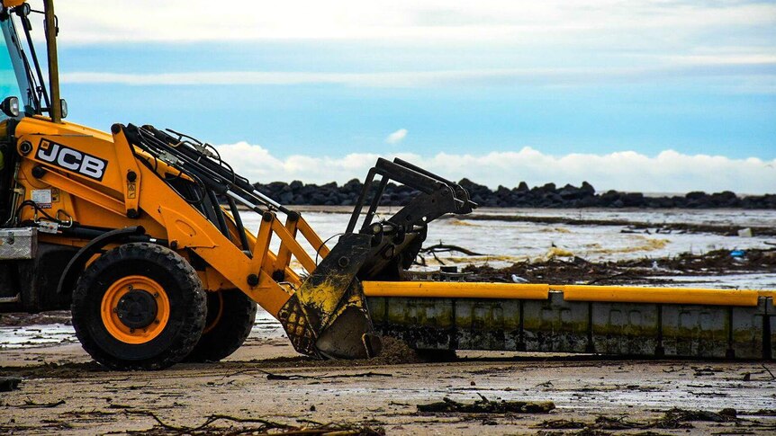 A front-end loader clears debris on a beach in Wynyard.