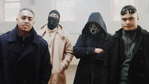 Four men in dark clothes, two in hoods, standing inside a church.