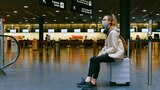 Woman with mask on sitting on luggage in an empty airport