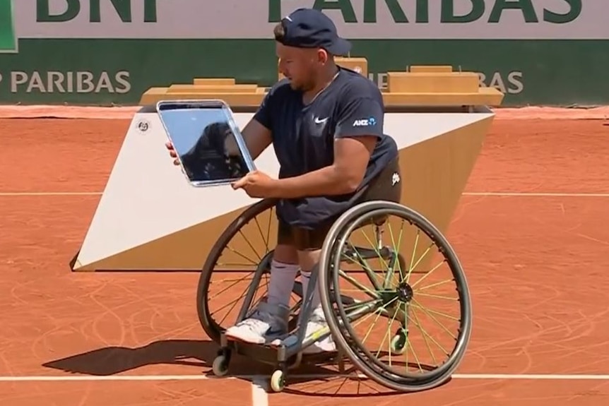 Dylan Alcott sits in his wheelchair and admires his trophy.