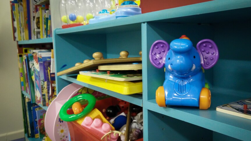A collection of children's books, toys and games stored in a blue bookshelf.