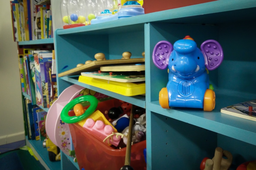 A collection of children's books, toys and games stored in a blue bookshelf.