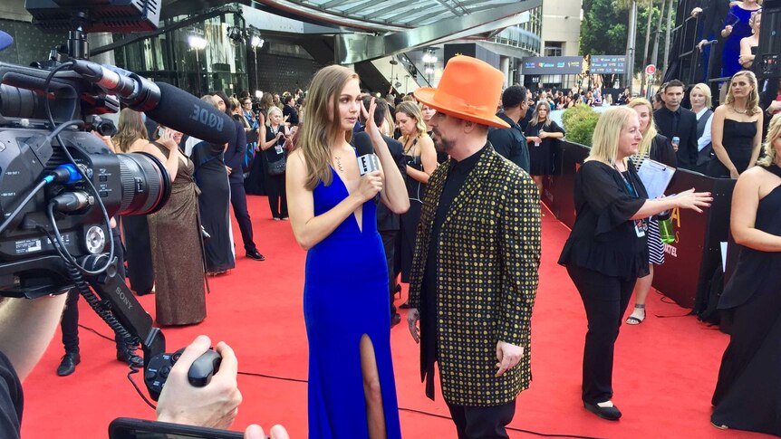 Boy George wearing an orange hat, getting interviewed on the red carpet at the AACTA awards.