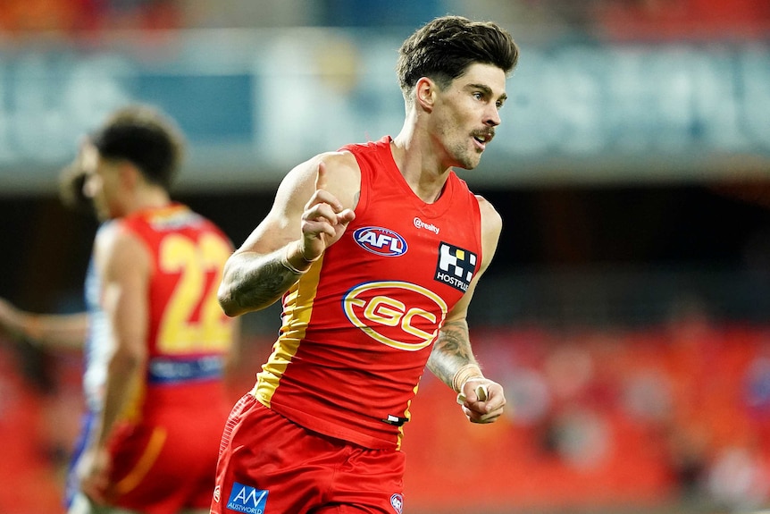A Gold Coast Suns AFL player points a finger on his right hand as he celebrates a goal against North Melbourne.