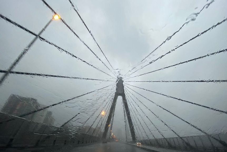 Heavy rain falls on a car windshield as it travels on the Anzac Bridge.