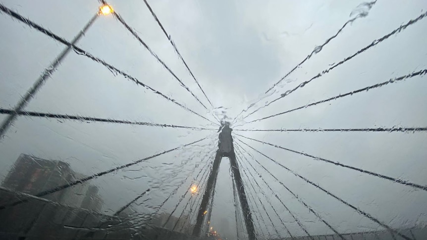 Heavy rain falls on a car windshield as it travels on the Anzac Bridge.