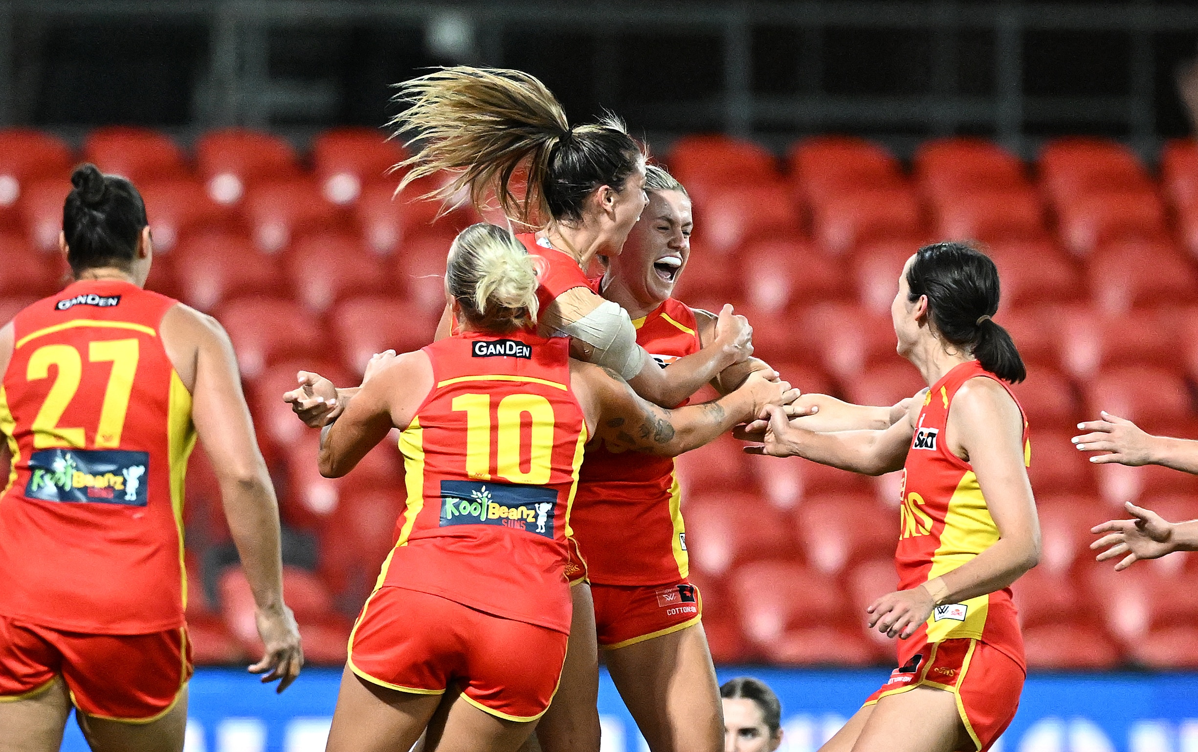 five women wearing red smiling and hugging on a football field