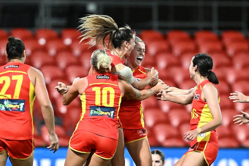 five women wearing red smiling and hugging on a football field