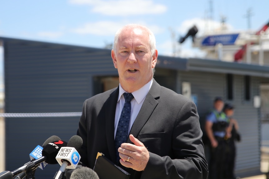 A white haired detective wears a suit as he addresses media 