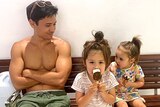 Seiji Armstrong sitting cross-armed with his two daughters in a story about why kids can prefer one parent and what to do.