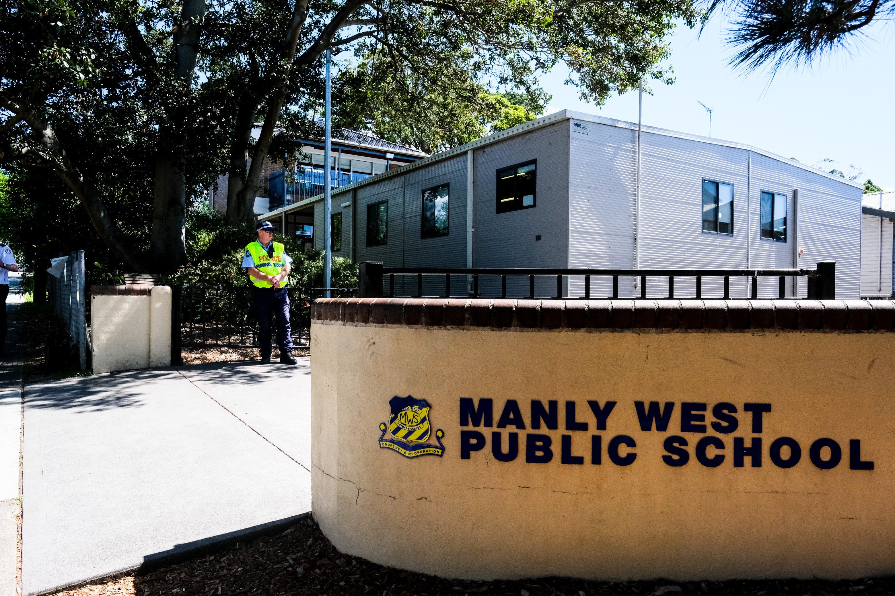 Man dressed in police officer uniform standing outside school building.