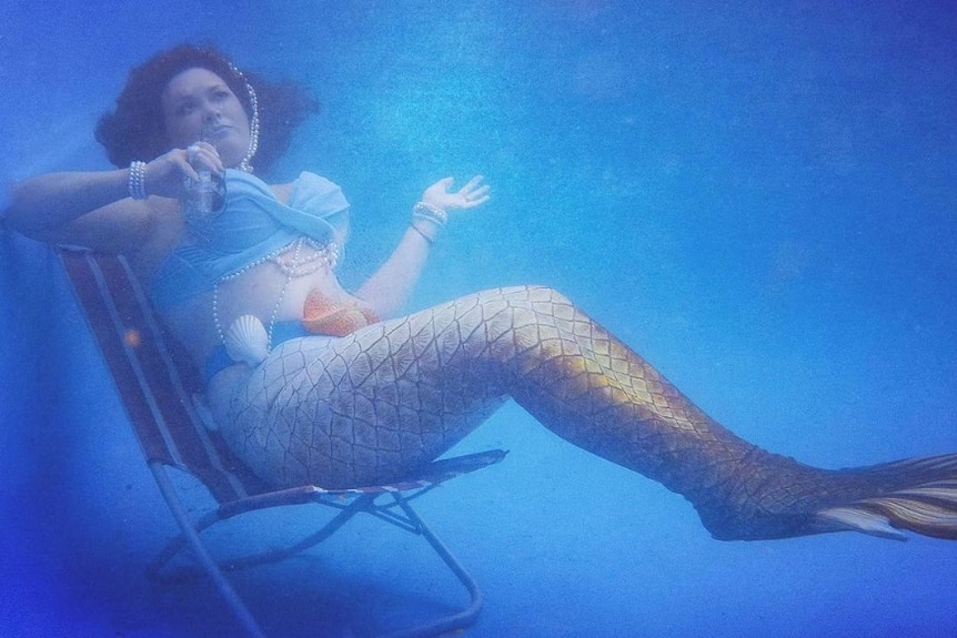 Nicola Robey aka Mermaid Naqulaan poses on a deckchair underwater.