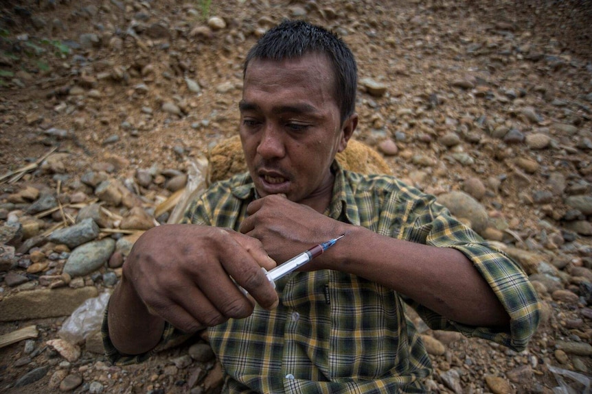A drug addict shoots heroin at the jade mining site in Myanmar