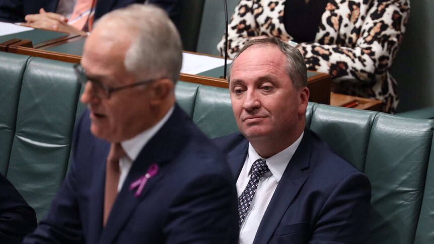 Barnaby Joyce, tight-lipped and staring blankly ahead, sits behind Malcolm Turnbull, who is out of focus in the foreground.
